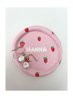 a pink plate with two pairs of earrings and the word hannah on it, sitting next to some strawberries