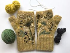 two knitted mittens with flowers and leaves on them next to a ball of yarn