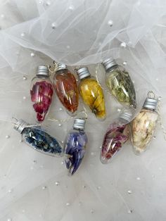 six glass ornaments with different colored flowers in them on a white cloth covered tablecloth