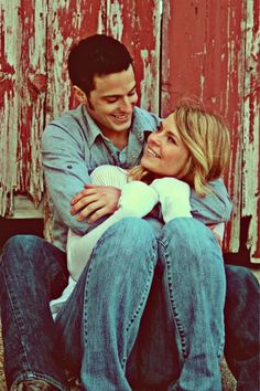 a man and woman sitting next to each other in front of an old red door