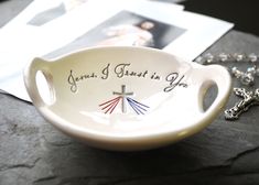 a small bowl with the words jesus christ is you on it and a rosary laying next to it