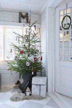 a small christmas tree in a room with white walls and flooring is decorated with ornaments