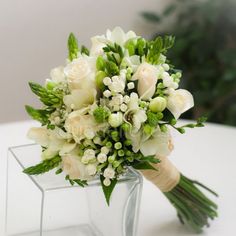 a bouquet of white flowers sits in a clear vase on a table with greenery