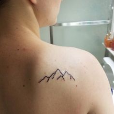 a woman with a tattoo on her shoulder and mountains in the back, behind her