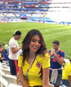 a woman in a yellow shirt is sitting on a bench at a soccer game and smiling