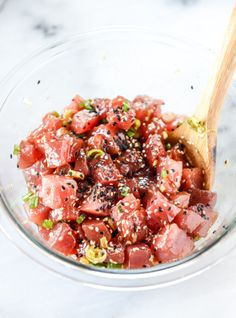 a glass bowl filled with diced meat and seasoning next to a wooden spoon