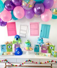 a table topped with cakes and balloons next to a wall filled with colorful decorations on top of it