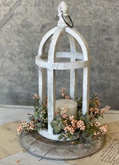 a candle is sitting in a white birdcage filled with flowers and greenery