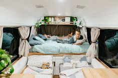 two people laying in the back of a camper van with beds and curtains open