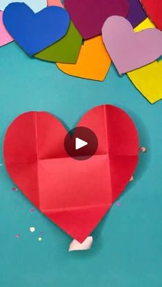 an origami heart surrounded by hearts and confetti on a blue background