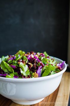 a white bowl filled with lettuce and red cabbage salad on top of a wooden table