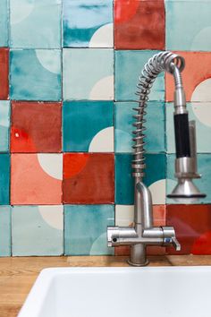 a kitchen sink with a faucet in front of a colorful tile backsplash