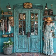 a woman standing in front of a blue door wearing a long dress and straw hat