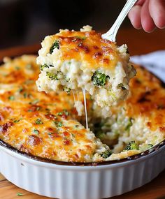 a close up of a casserole with broccoli and cheese being lifted from it