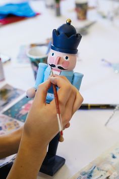 a person is painting a toy soldier with a paintbrush in their hand and holding a pencil