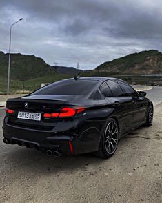 a black bmw is parked on the side of the road in front of some hills