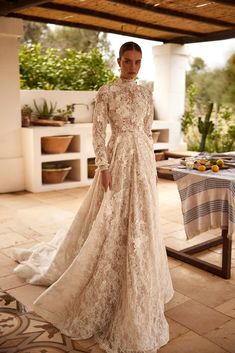 a woman in a wedding dress standing on a patio with an open table and potted plants behind her