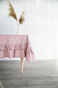 a table topped with a vase filled with dry grass sitting on top of a wooden floor