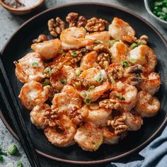 a black plate topped with shrimp and rice next to chopsticks on a table