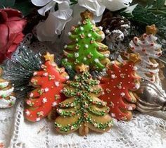 christmas cookies decorated like trees on a lace tablecloth with flowers in the back ground