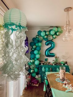 a room filled with balloons and tables covered in blue and green decorations for a two year old birthday party