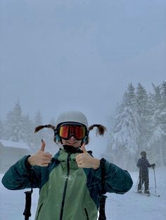 a woman giving the thumbs up sign while standing in the snow with skis on