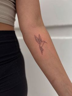 a woman's arm with a small bird tattoo on the left side of her arm