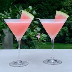 two martini glasses with watermelon garnish sit on a white table outside