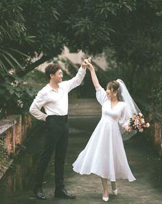 a bride and groom holding hands while standing next to each other in front of trees