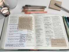 an open book with writing on it next to some pens and markers, glasses and a candle