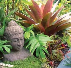 a buddha statue sitting in the middle of a lush green garden filled with flowers and plants