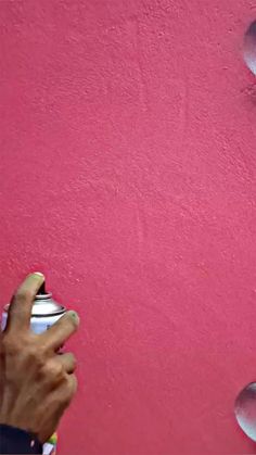 a person holding a cup in front of a pink wall with spoons on it