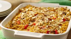 a casserole dish filled with noodles and vegetables, topped with sliced almonds