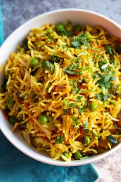 a white bowl filled with yellow rice and green beans on top of a blue napkin