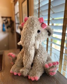 a stuffed elephant sitting on top of a wooden table next to a window covered in blinds