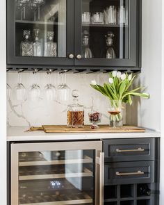 a kitchen with wine glasses and bottles on the counter, next to an open cabinet