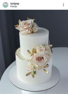 a three tiered white cake with flowers on the top and gold trimmings