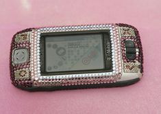 a cell phone covered in swarong and beads on a pink surface with a button