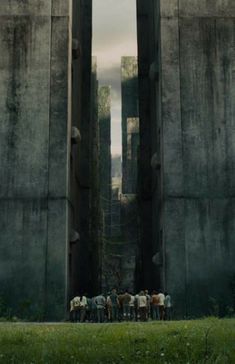 a group of people standing on top of a lush green field next to tall concrete structures