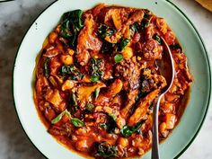 a white plate topped with meat and spinach covered in tomato sauce next to bread