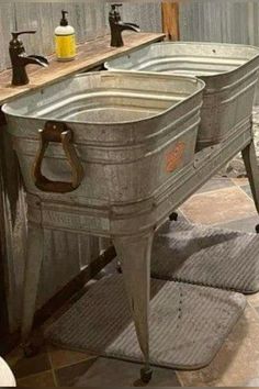 two metal sinks sitting next to each other on top of a tiled floor in a bathroom