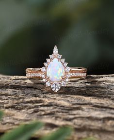 a white opal and diamond ring sitting on top of a piece of wood