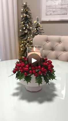 a christmas centerpiece on a table with a lit candle and holly berries in it