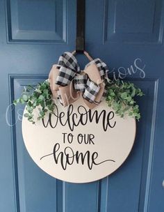 welcome to our home sign hanging on the front door with greenery and bow tie