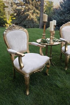 two chairs and a table in the grass with candles on top of them, next to each other