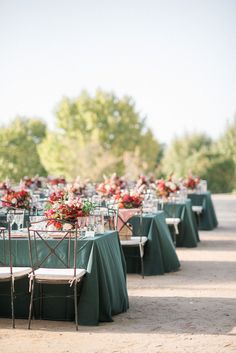 tables set up with green linens and red centerpieces for an outdoor wedding