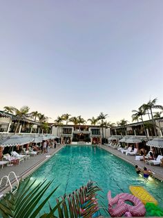 an outdoor swimming pool surrounded by lawn chairs and umbrellas with palm trees in the background