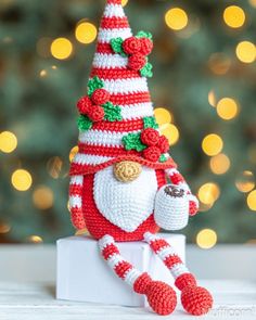 a crocheted santa clause doll sitting on top of a white box next to a christmas tree