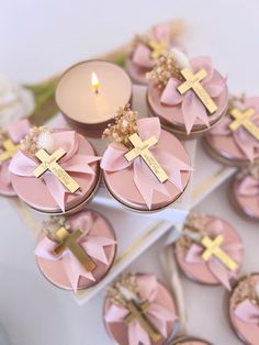 pink cupcakes with gold crosses on them are sitting next to a lit candle