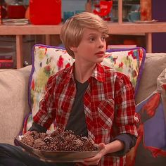 a young boy sitting on a couch holding a tray of food